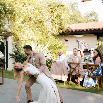 A groom dipping his bride for a kiss at an outdoor reception, with DJ Paul in the background