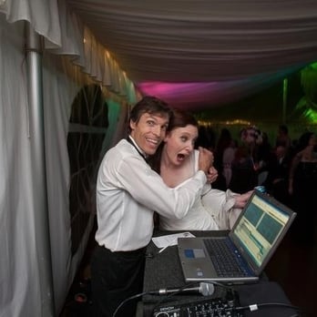 Paul sharing a playful moment with the bride at the DJ booth under colorful uplighting