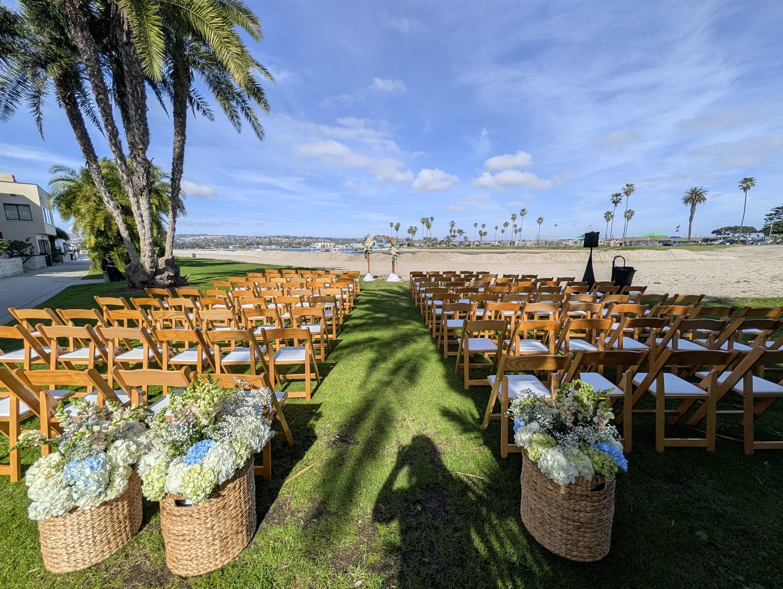Bayfront wedding ceremony setup with wood chairs and floral baskets at Mission Beach