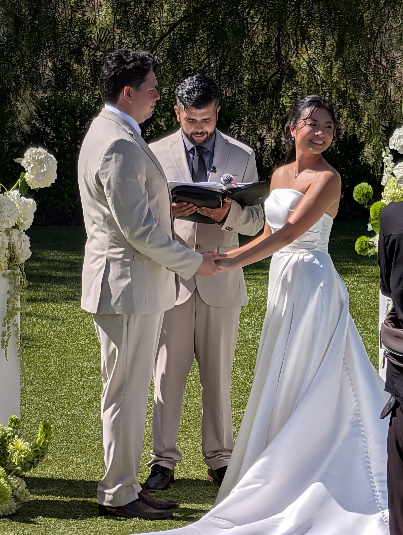 Bride and groom holding hands at the altar while the officiant reads from a discreetly mic'd binder