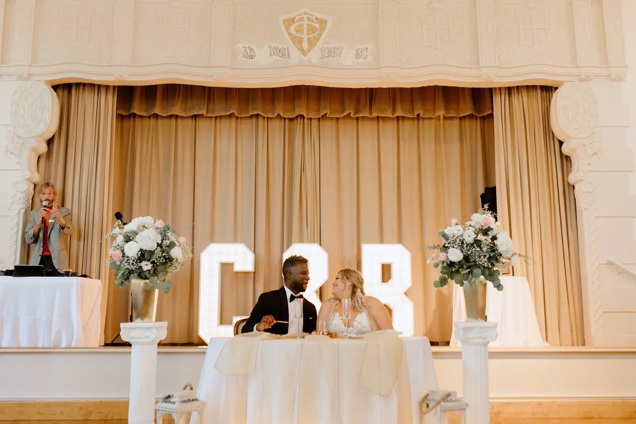 Bride and groom at their sweetheart table on the historic stage at The Thursday Club in Point Loma, with Paul MC'ing